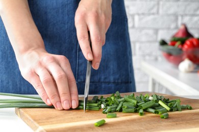 Photo of Woman cutting green spring onion on wooden board, closeup
