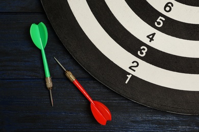 Photo of Dart board with color arrows on black wooden background, top view