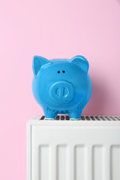Photo of Piggy bank on heating radiator against pink background