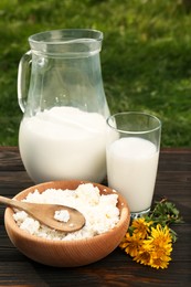 Photo of Tasty fresh milk and cottage cheese on wooden table outdoors