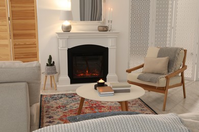 Photo of Beautiful fireplace, armchair and table in living room. Interior design