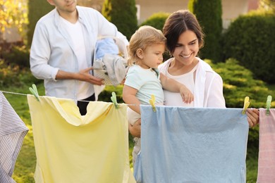 Photo of Happy family hanging clothes with clothespins on washing line for drying in backyard