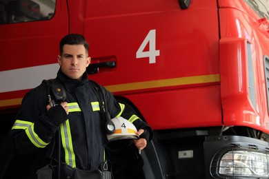 Photo of Portrait of firefighter in uniform with helmet near fire truck at station, space for text