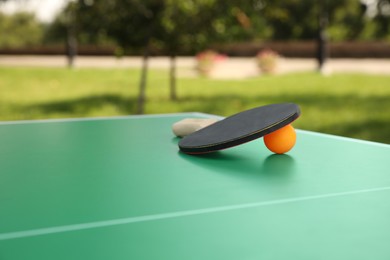 Photo of Racket and ball on green ping pong table outdoors. Space for text