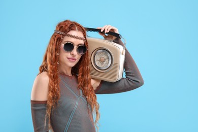 Photo of Stylish young hippie woman with retro radio receiver on light blue background
