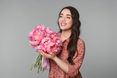 Photo of Beautiful young woman with bouquet of peonies on light grey background