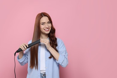 Photo of Beautiful woman using hair iron on pink background, space for text