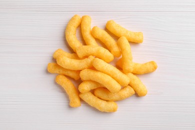 Photo of Heap of tasty cheesy corn puffs on white wooden table, flat lay