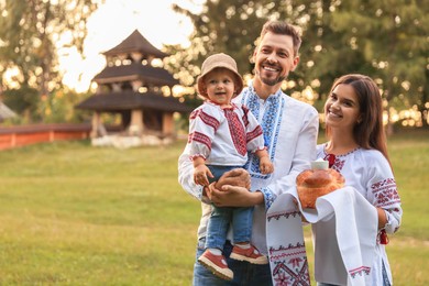 Photo of Happy cute family in embroidered Ukrainian shirts with korovai bread on sunny day. Space for text