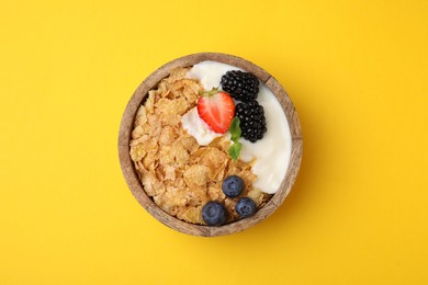 Photo of Delicious crispy cornflakes, yogurt and fresh berries in bowl on yellow background, top view. Healthy breakfast