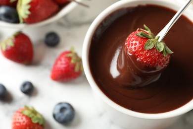 Photo of Dipping strawberry into fondue pot with chocolate on white table, top view