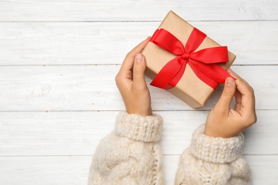 Photo of Young woman holding Christmas gift on white wooden background, top view. Space for text