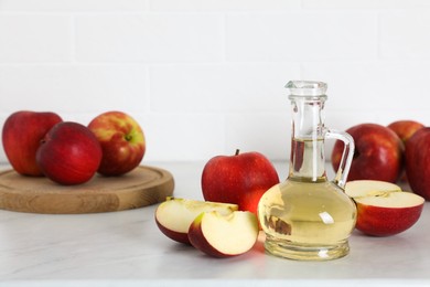 Photo of Natural apple vinegar and fresh fruits on white marble table. Space for text