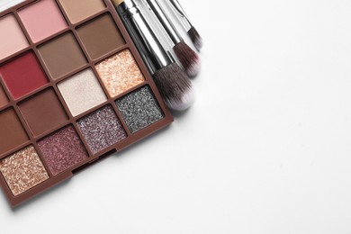 Photo of Beautiful eye shadow palette and brushes on white table, flat lay. Space for text