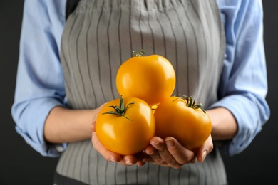 Photo of Woman holding yellow tomatoes on dark background, closeup