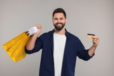 Photo of Happy man with many paper shopping bags showing credit card on grey background