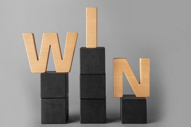 Photo of Word WIN made with wooden letters on toy blocks against grey background. Victory concept