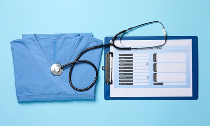 Photo of Medical uniform, stethoscope and clipboard on light blue background, flat lay