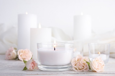 Photo of Composition with burning aromatic candle and roses on wooden table