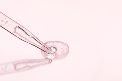 Photo of Glass pipette and transparent liquid on light pink background, closeup. Space for text