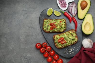 Photo of Slices of bread with tasty guacamole and ingredients on grey table, flat lay. Space for text