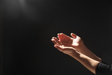 Photo of Religion. Woman with open palms praying on black background, closeup. Space for text