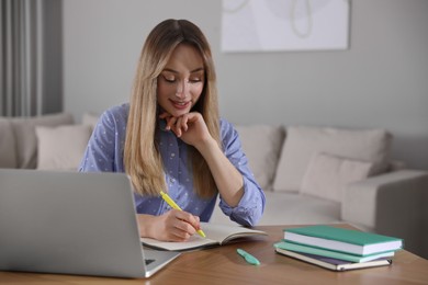 Photo of Young woman writing down notes during webinar at table in room