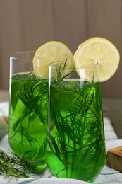 Photo of Glasses of refreshing tarragon drink with lemon slices on table, closeup