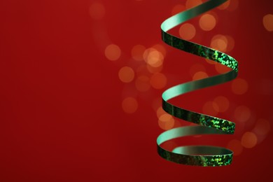 Photo of Shiny green serpentine streamer against blurred lights, closeup. Space for text