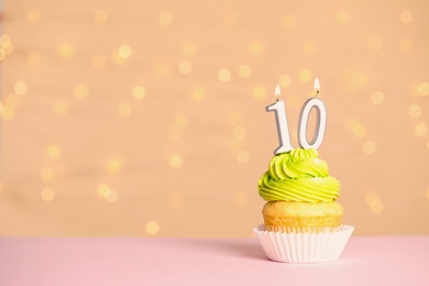Photo of Birthday cupcake with number ten candle on table against festive lights, space for text