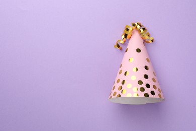 Photo of One pink party hat with serpentine streamers on purple background, top view. Space for text