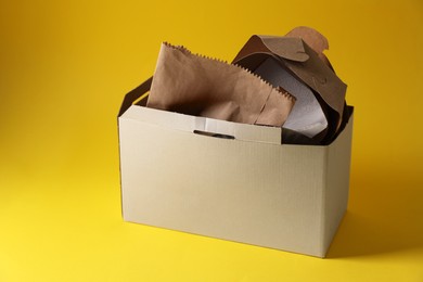 Photo of Box with waste paper on yellow background