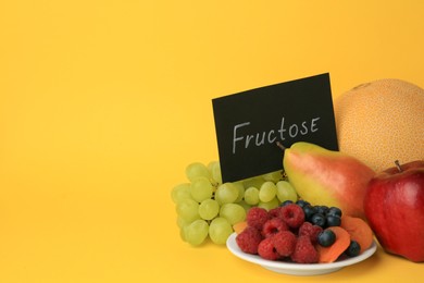 Photo of Card with word Fructose, delicious ripe fruits, berries and dried apricots on yellow background, space for text
