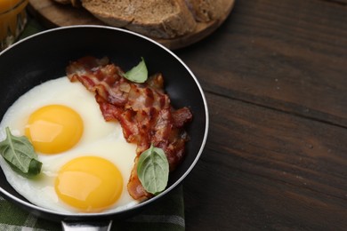 Photo of Fried eggs, bacon and basil in frying pan on wooden table, space for text