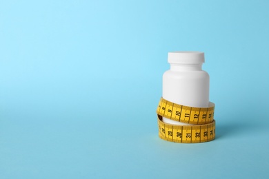 Bottle of weight loss pills with measuring tape on color background. Space for text