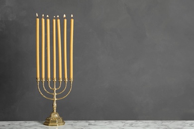 Photo of Golden menorah with burning candles on table against grey background, space for text