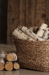 Photo of Wicker basket with cut firewood on floor indoors