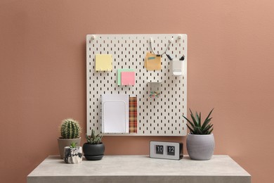 Photo of White notice board with notes and stationery hanging on pink wall over table indoors