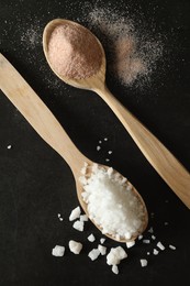 Photo of Different types of organic salt in spoons on black table, flat lay