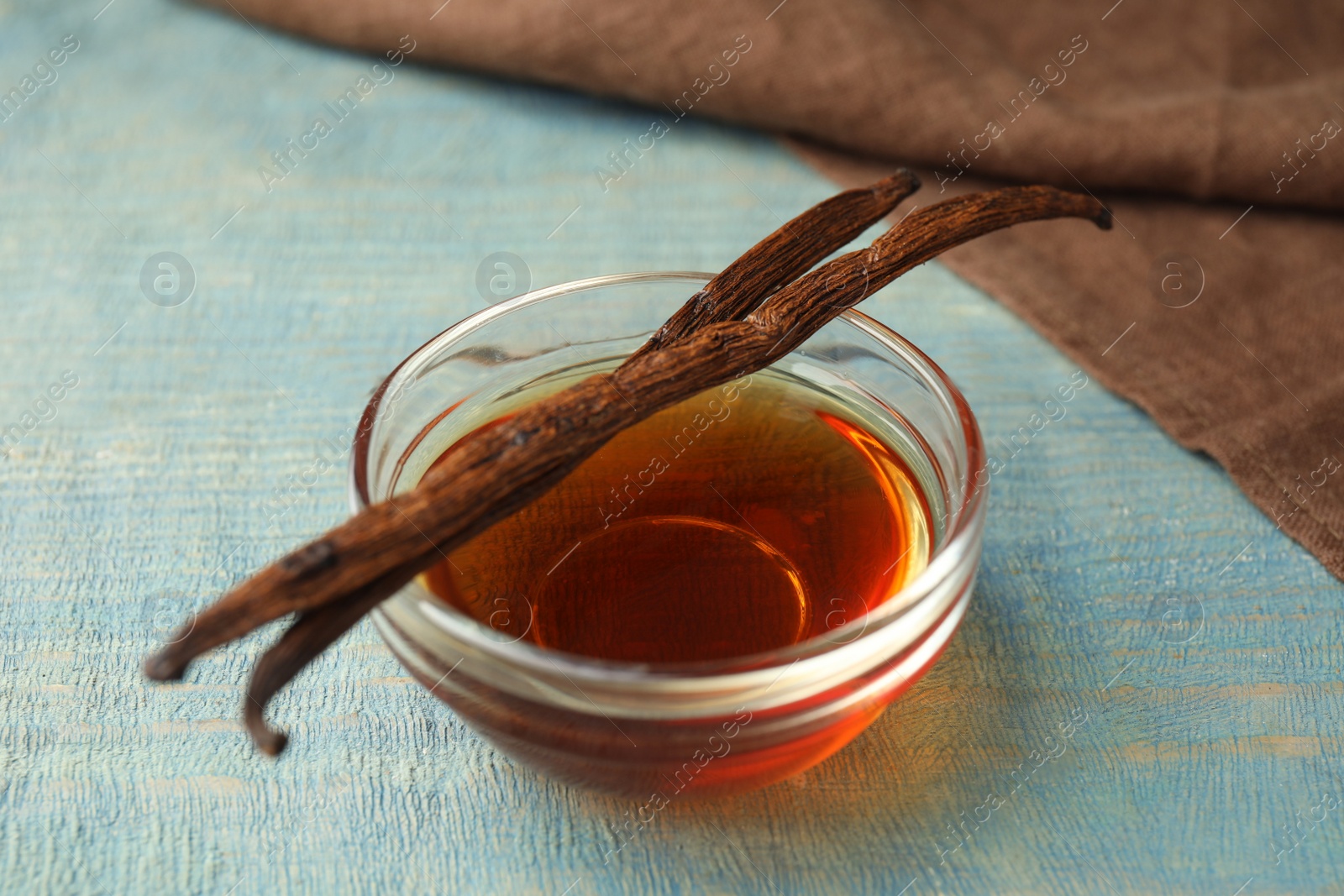 Photo of Aromatic homemade vanilla extract on light blue  wooden table, closeup