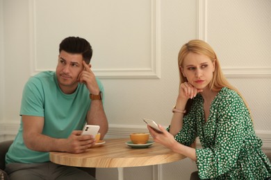 Photo of Displeased man and young woman with smartphones in cafe. Failed first date