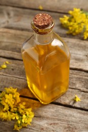 Photo of Rapeseed oil in glass bottle and beautiful yellow flowers on wooden table, closeup