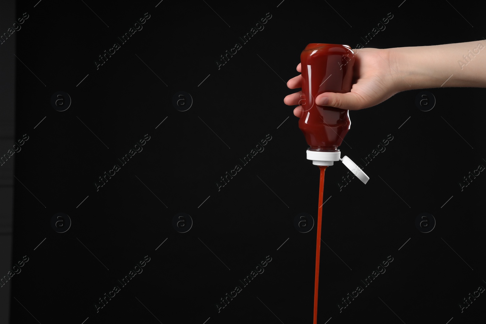 Photo of Woman pouring tasty ketchup from bottle on black background, closeup. Space for text