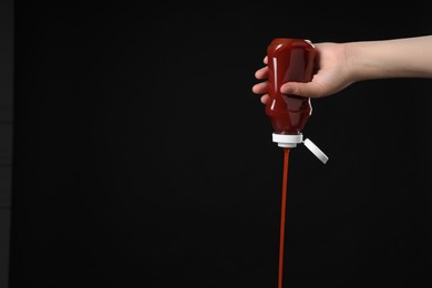 Photo of Woman pouring tasty ketchup from bottle on black background, closeup. Space for text