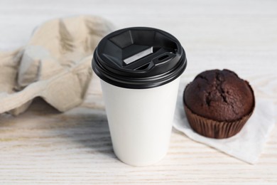 Photo of Paper cup with black lid and muffin on white wooden table, closeup. Coffee to go
