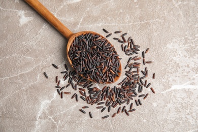 Photo of Spoon with uncooked black rice on grey background, top view