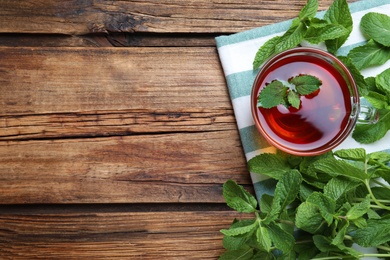 Photo of Cup with hot aromatic mint tea and fresh leaves on wooden table, flat lay. Space for text