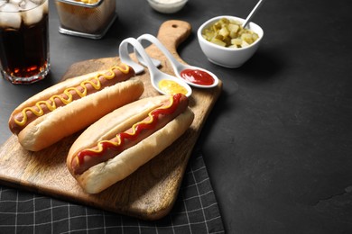 Photo of Fresh delicious hot dogs with sauces served on black table. Space for text