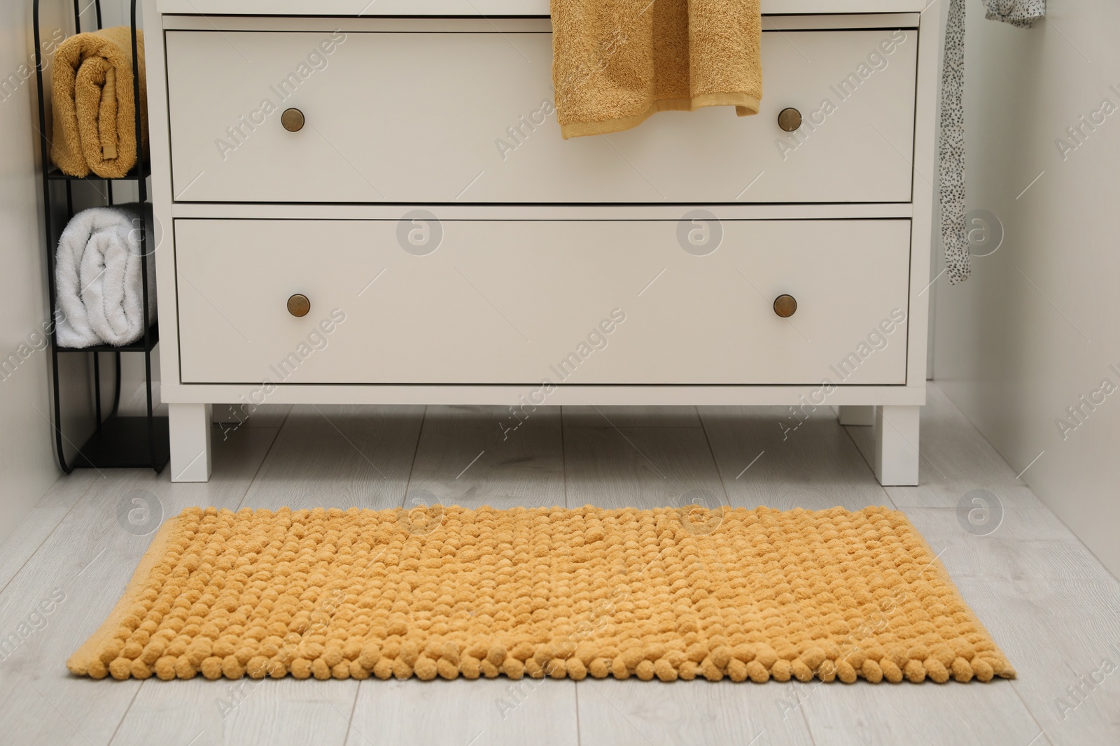 Photo of Orange bath mat near chest of drawers indoors