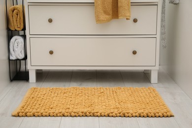 Orange bath mat near chest of drawers indoors